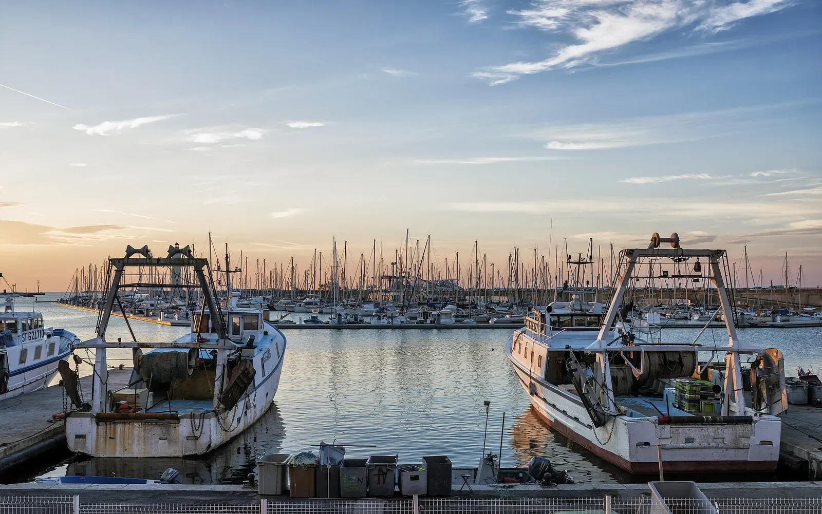Two fishing trawlers moored in front of a marina in Sète harbour at golden hour