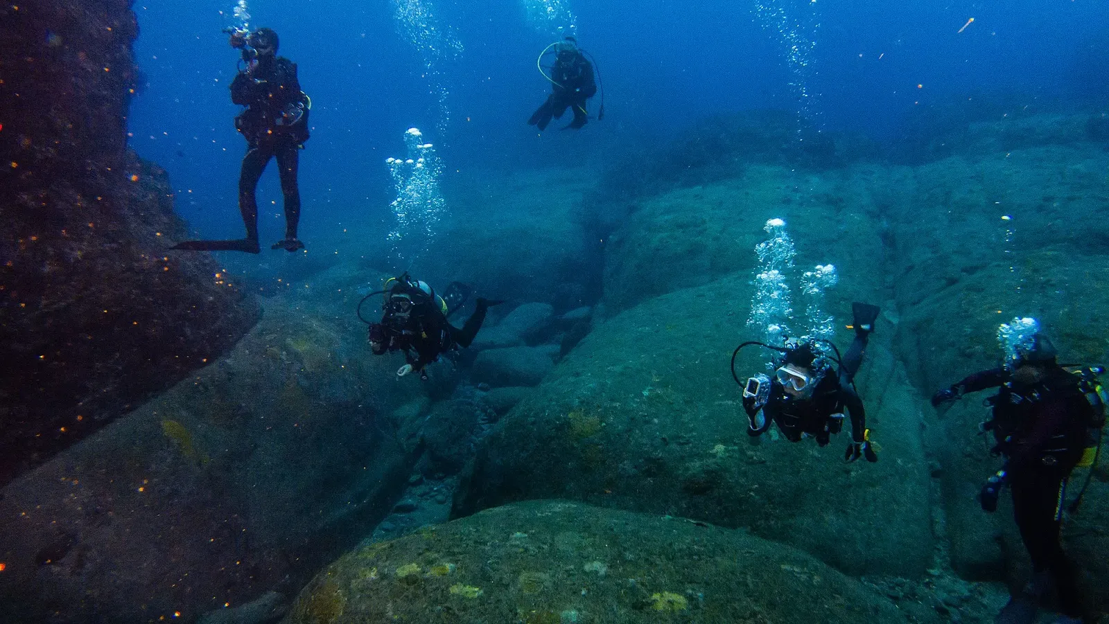 Divers hover over angular submerged rock terraces at the Yonaguni Monument dive site.