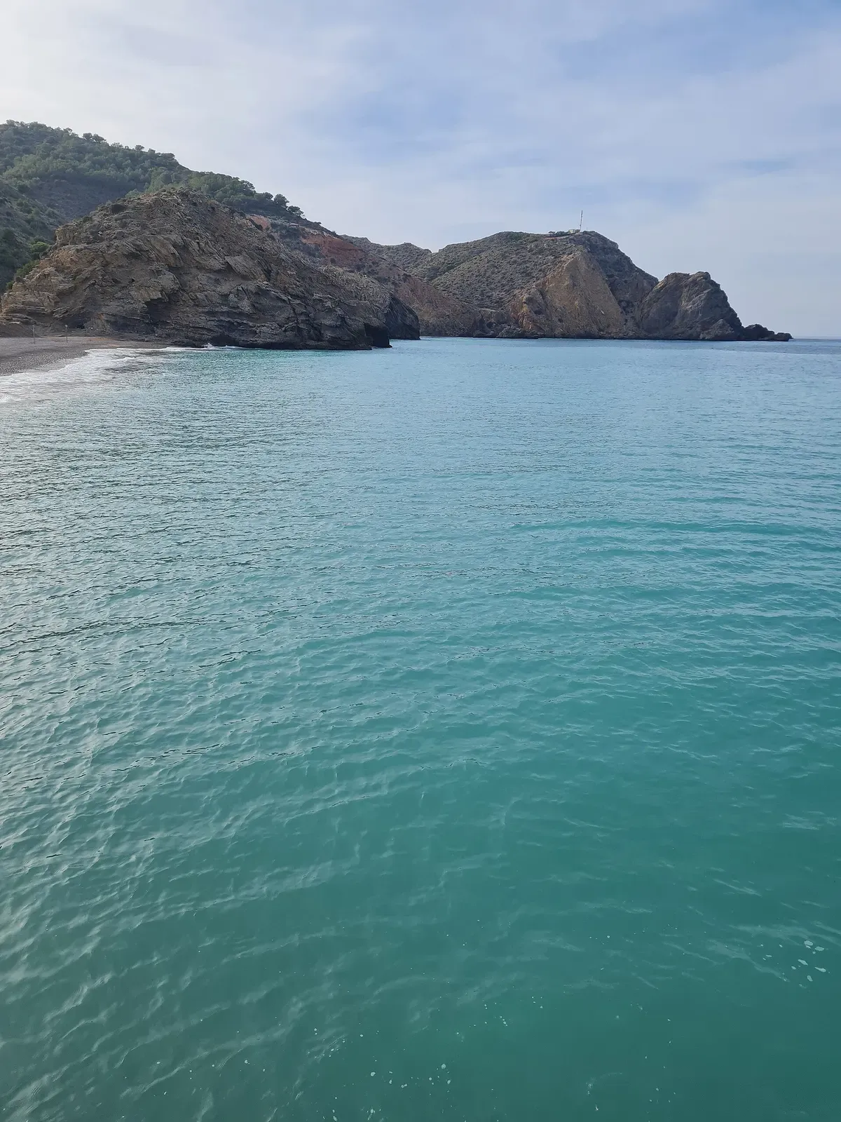 Clear turquoise water in a bay framed by rocky brown headlands and a small beach — Al Hoceima
