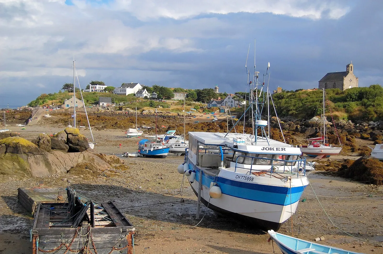 Blue and white fishing boat resting on the seabed at low tide, cottages on the shore behind — Chausey Islands & Granville