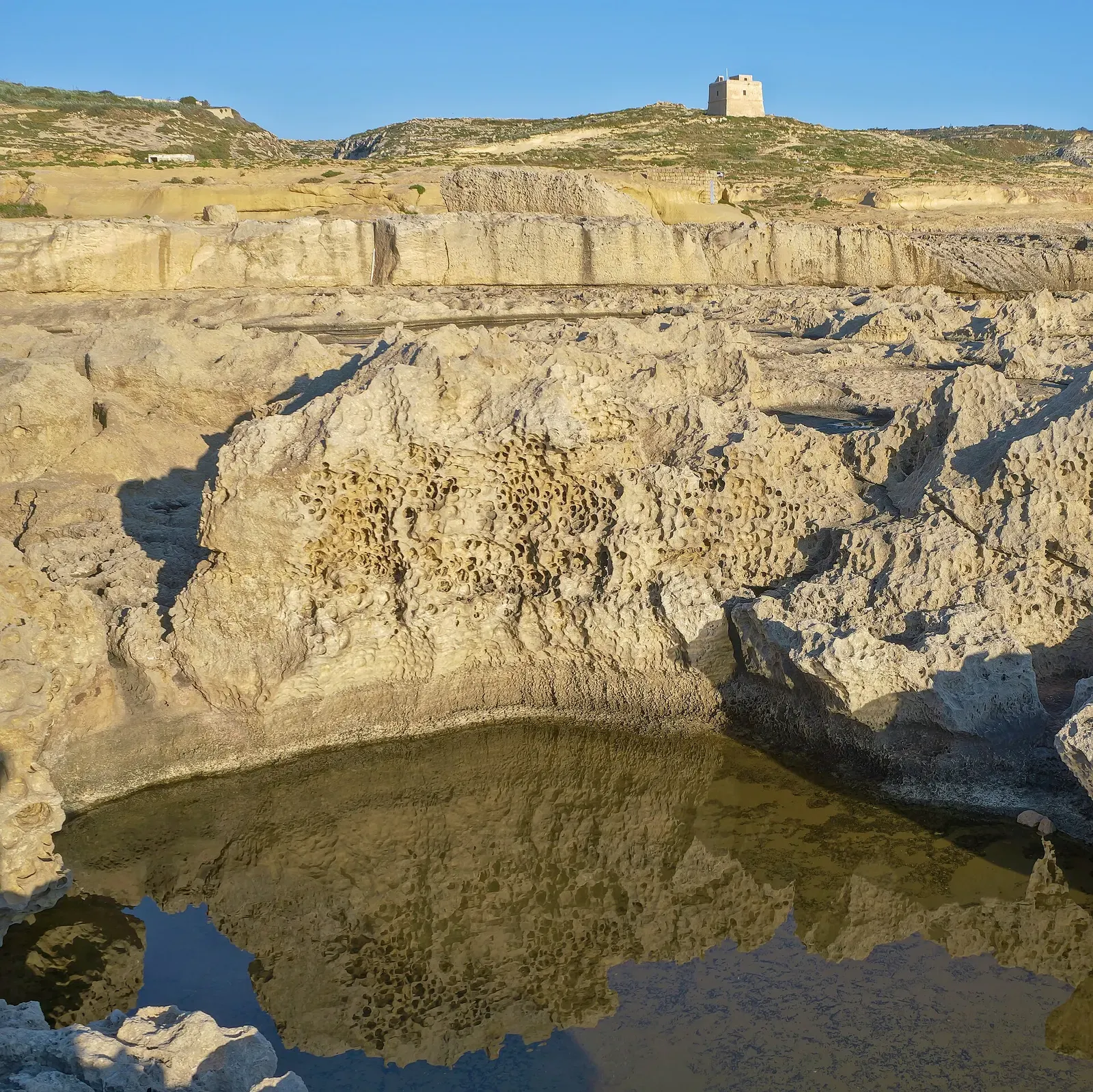 Rock pool at Dwejra with a Knights-era watchtower on the skyline above the coastline — Blue Hole & Inland Sea, Gozo & Malta