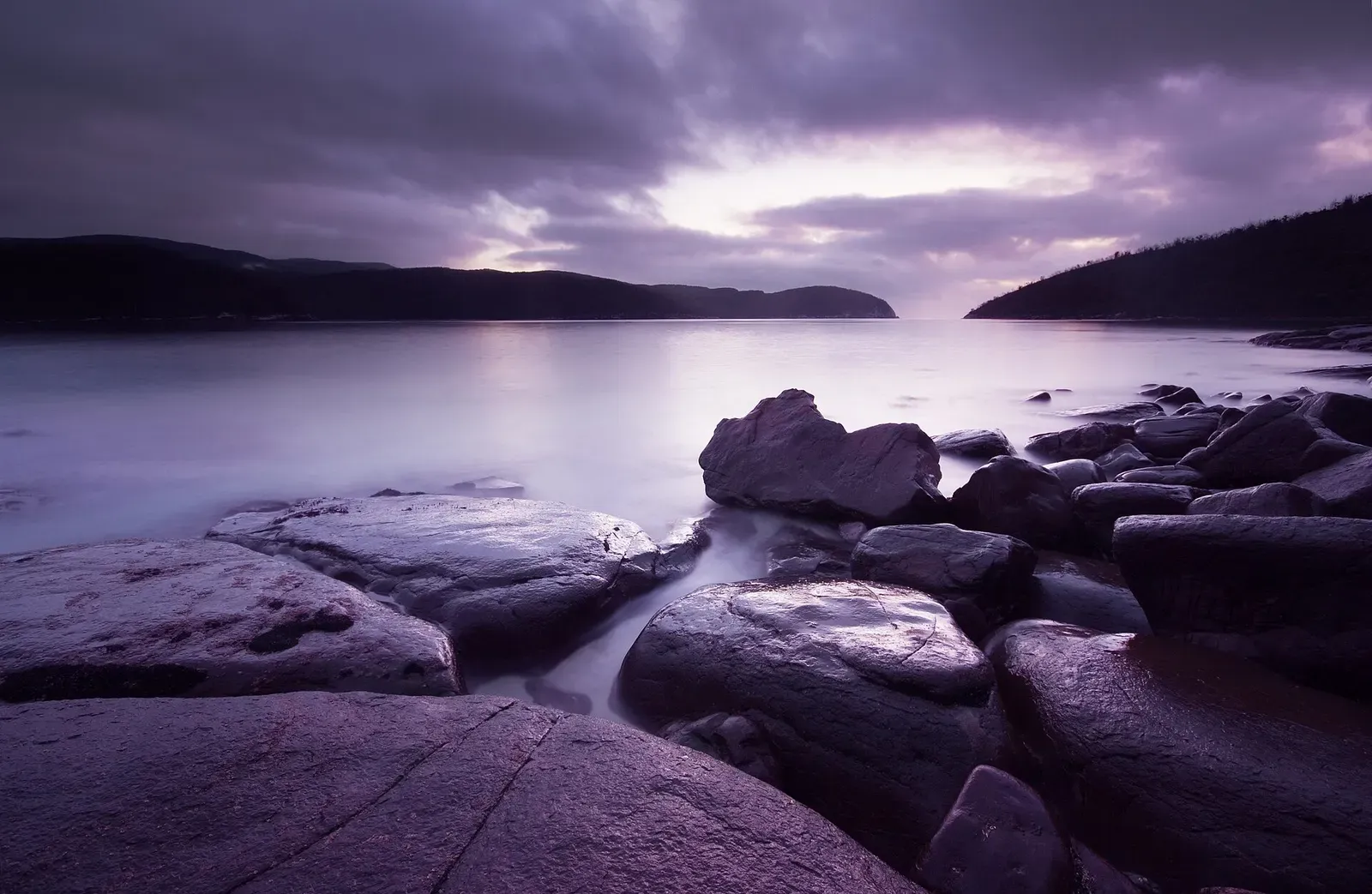 Dark rocky shoreline of Fortescue Bay at dawn with soft violet sky reflected on calm water — Eaglehawk Neck