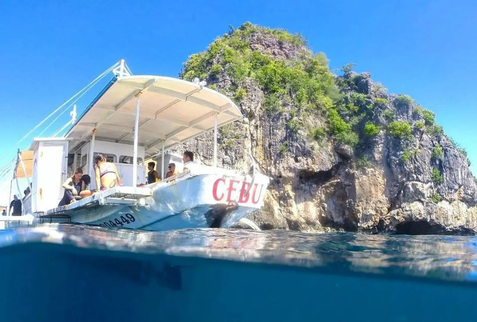 Dive boat moored beside Gato Island's limestone cliffs with divers boarding — Malapascua