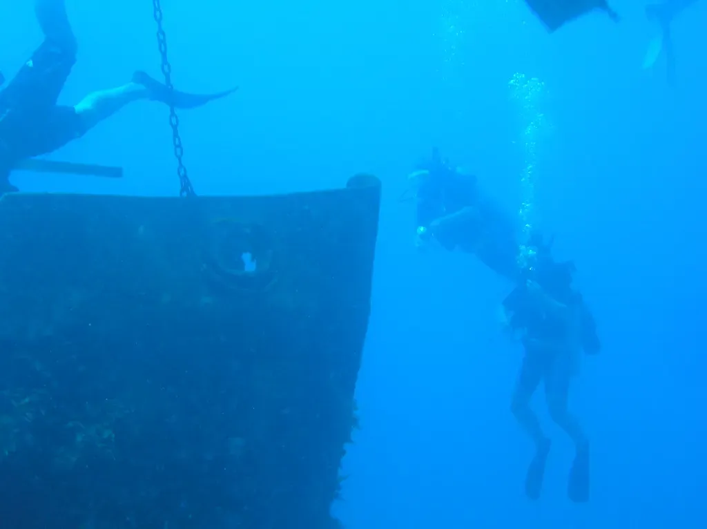 Silhouette of the wreck's hull section with a diver hovering alongside in blue water — Halliburton Wreck, Utila