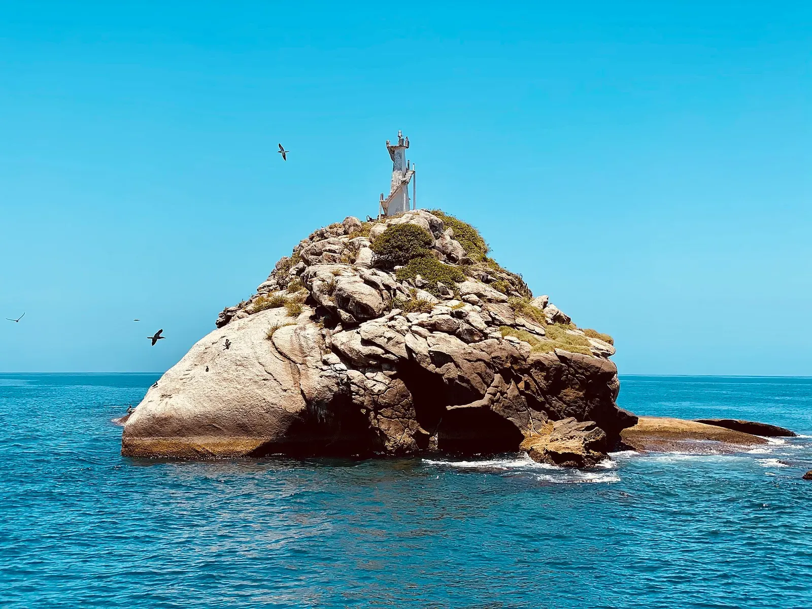 Small rocky islet topped by a white lighthouse structure with seabirds flying overhead — Alcatrazes Archipelago
