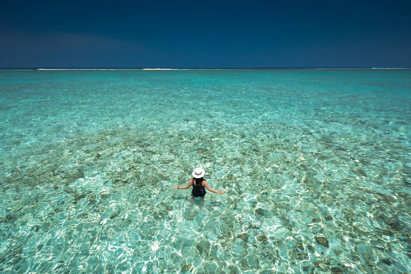 A person wading through shallow, clear turquoise water off Taj Exotica in South Malé Atoll