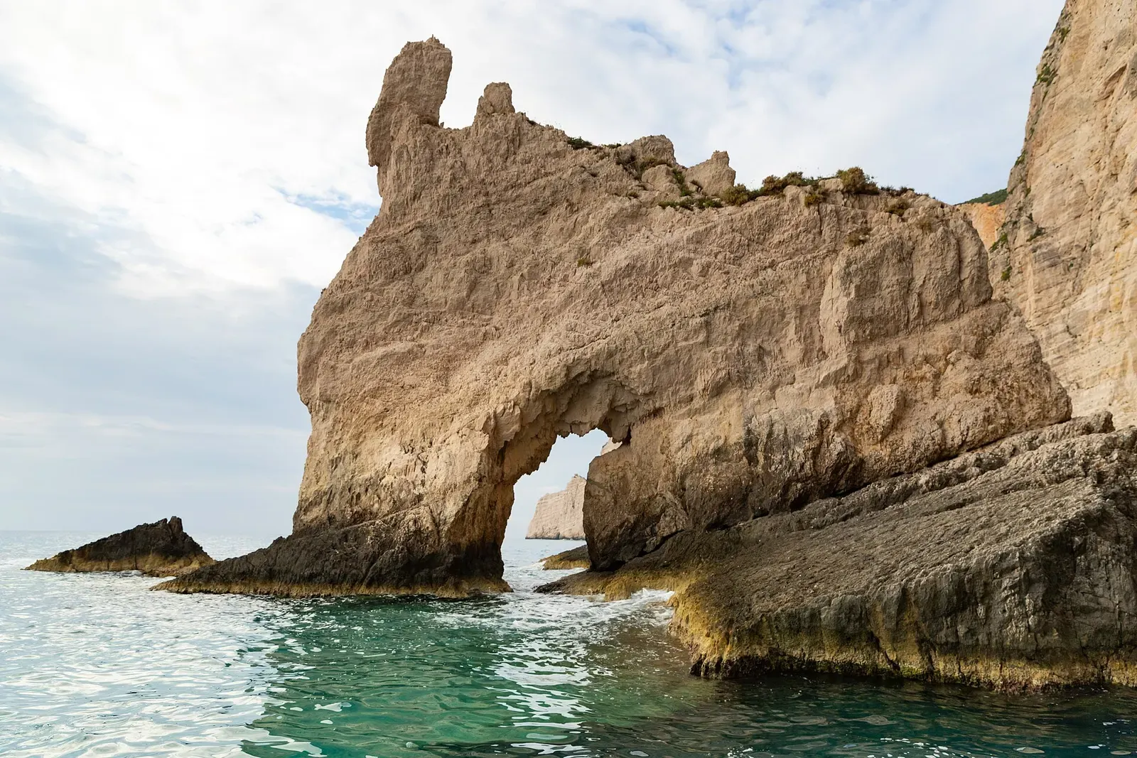 A tall limestone sea arch rises from turquoise water on the Zakynthos coast.
