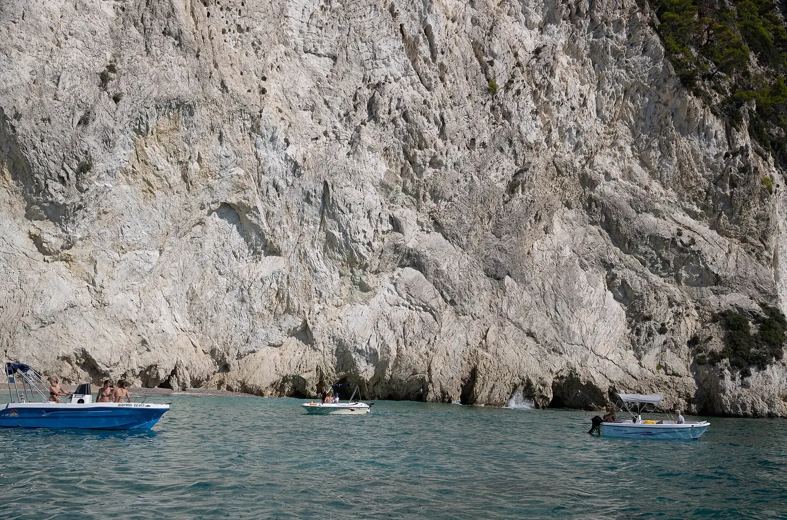 A sea cave and cliff face at Marathonisi island, with small boats anchored below.