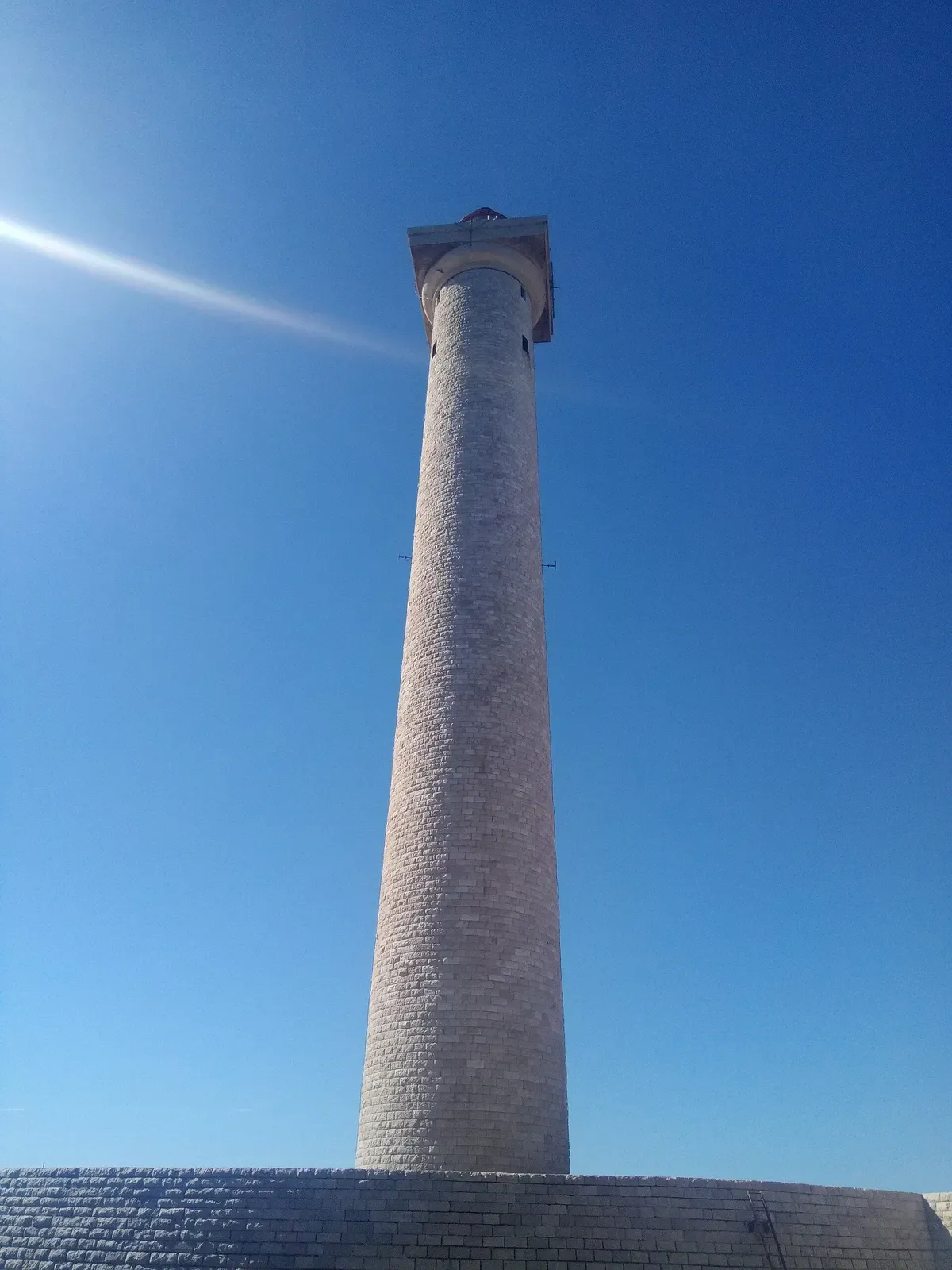 Looking straight up the tapered stone shaft of the Planier lighthouse against a clear blue sky — Le Planier, Marseille