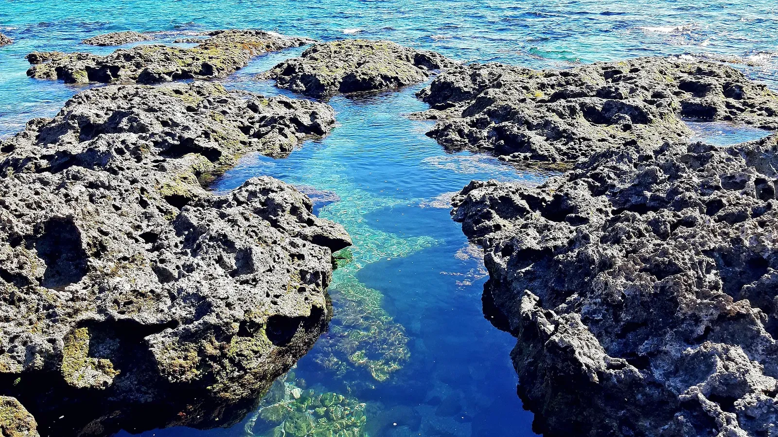 A narrow channel of clear blue water cuts through coral-rock coastline at Siangjiao Bay — Kenting.