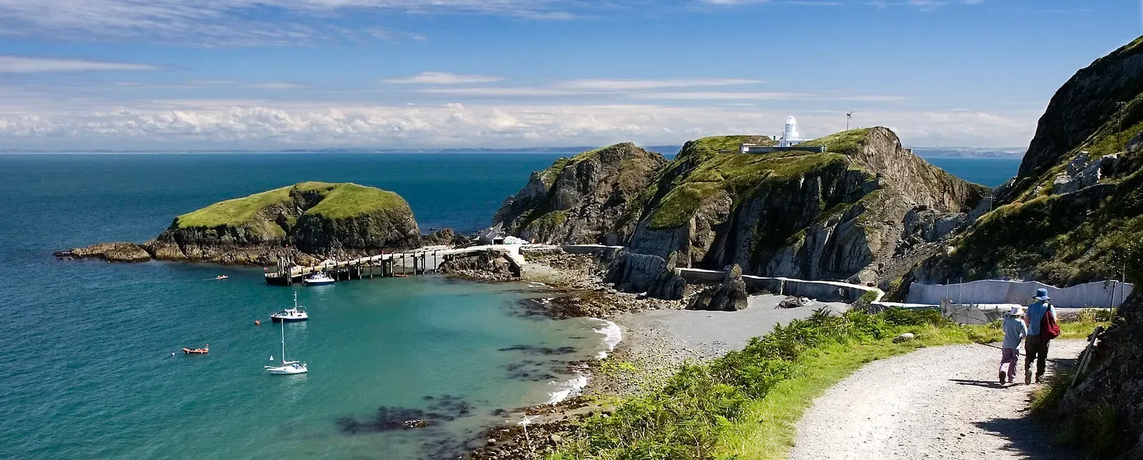 Panorama of Lundy's landing bay with a jetty, moored yachts, a shingle beach, Rat Island and the church on the headland above — Lundy Island