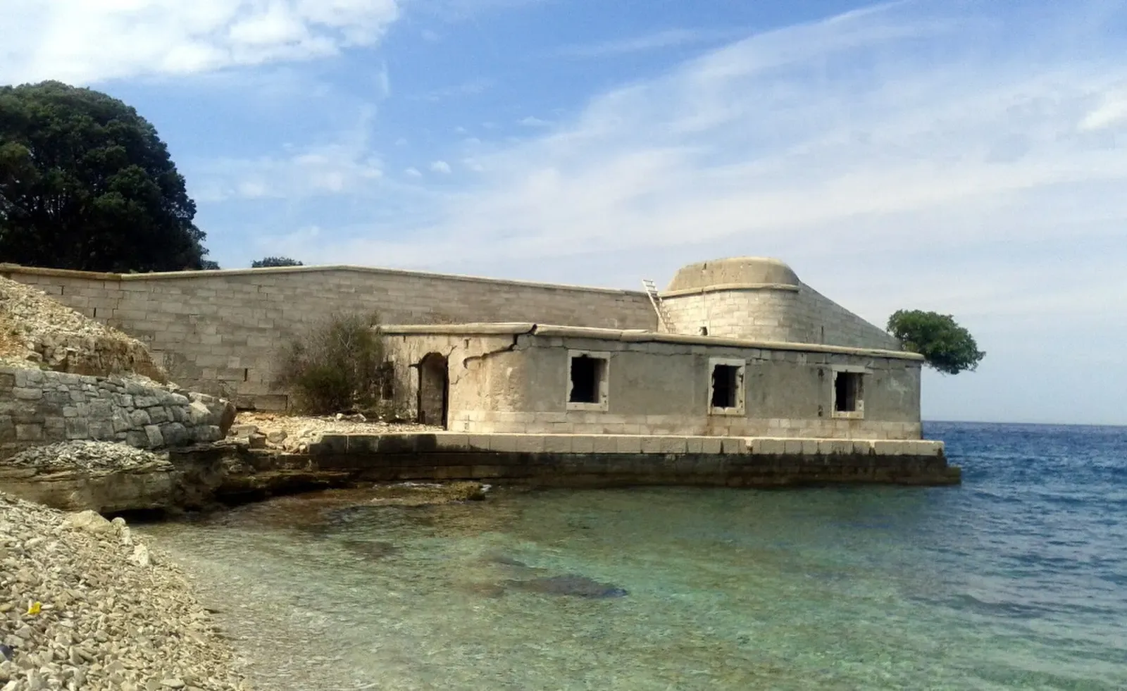 Concrete Austro-Hungarian torpedo-station building at the waterline over shallow green water