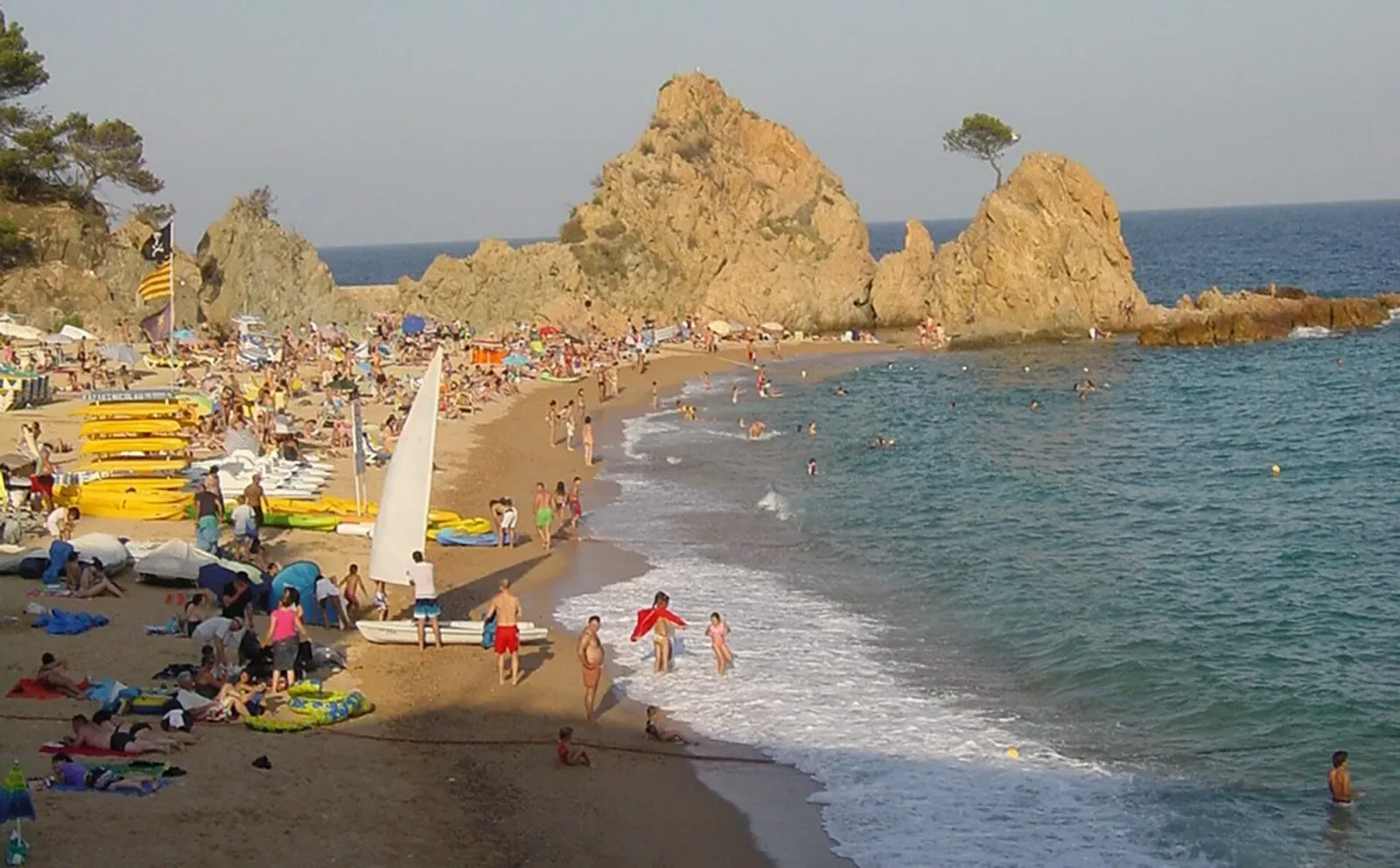 Swimmers and a small sailboat on the sand at Mar Menuda beach, with the rocky point behind.