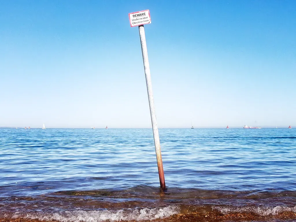 A warning sign for an underwater obstruction rising from the sea at Greenhill Beach, Weymouth