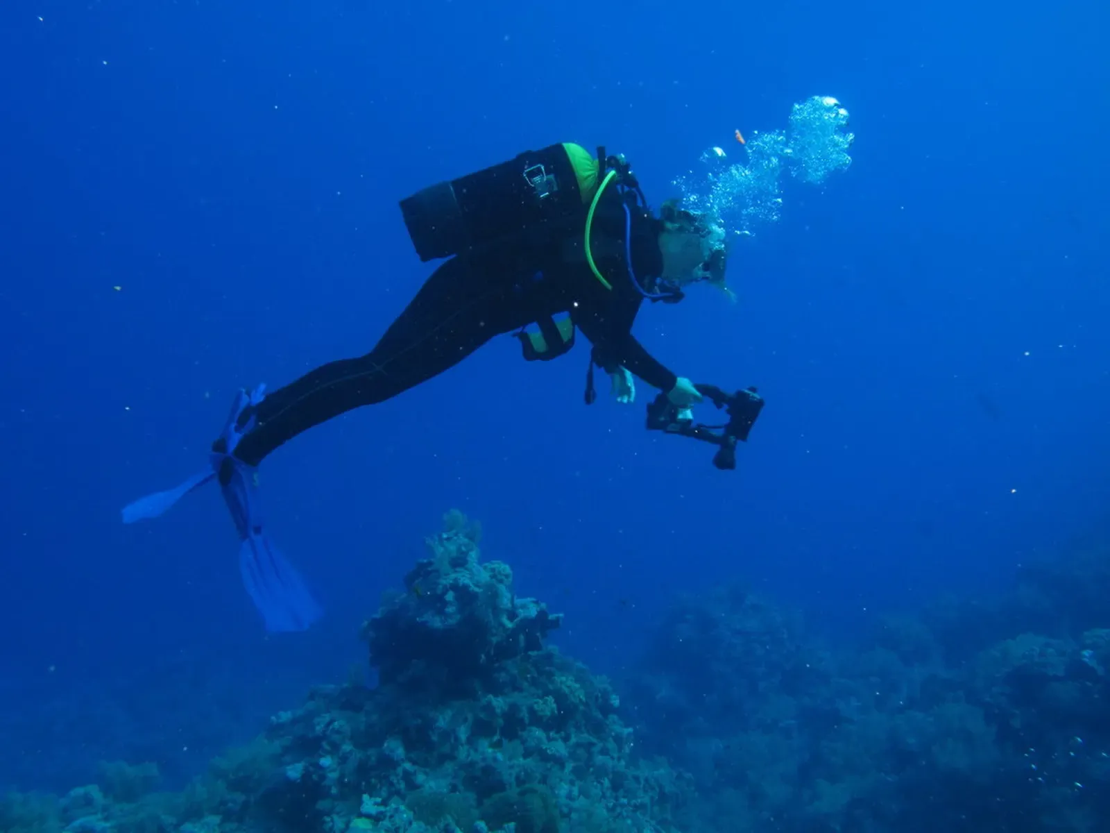 A diver trailing bubbles glides over open blue water near Gota Kebir — St John's Reefs
