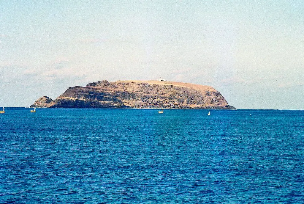 The islet Ilhéu de Cima off Porto Santo seen across open water, with small boats near the shoreline