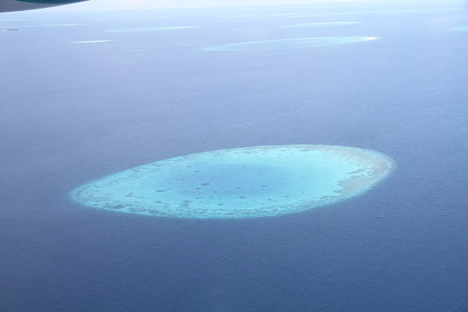 Aerial view of an oval turquoise reef lagoon surrounded by deep water