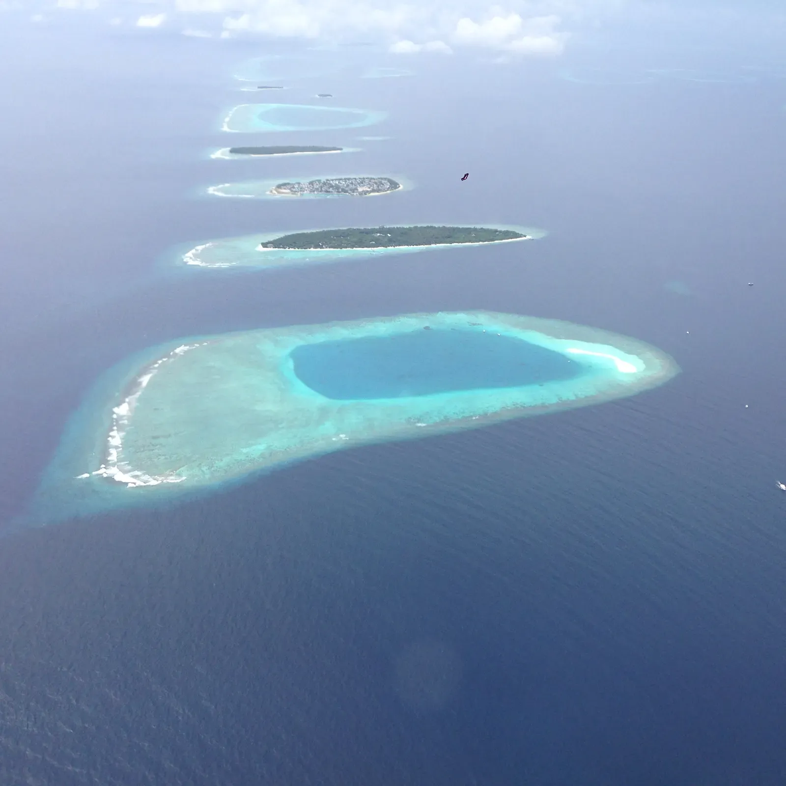 Aerial view of a chain of reef islands enclosing a shallow turquoise lagoon — Baa Atoll & Hanifaru