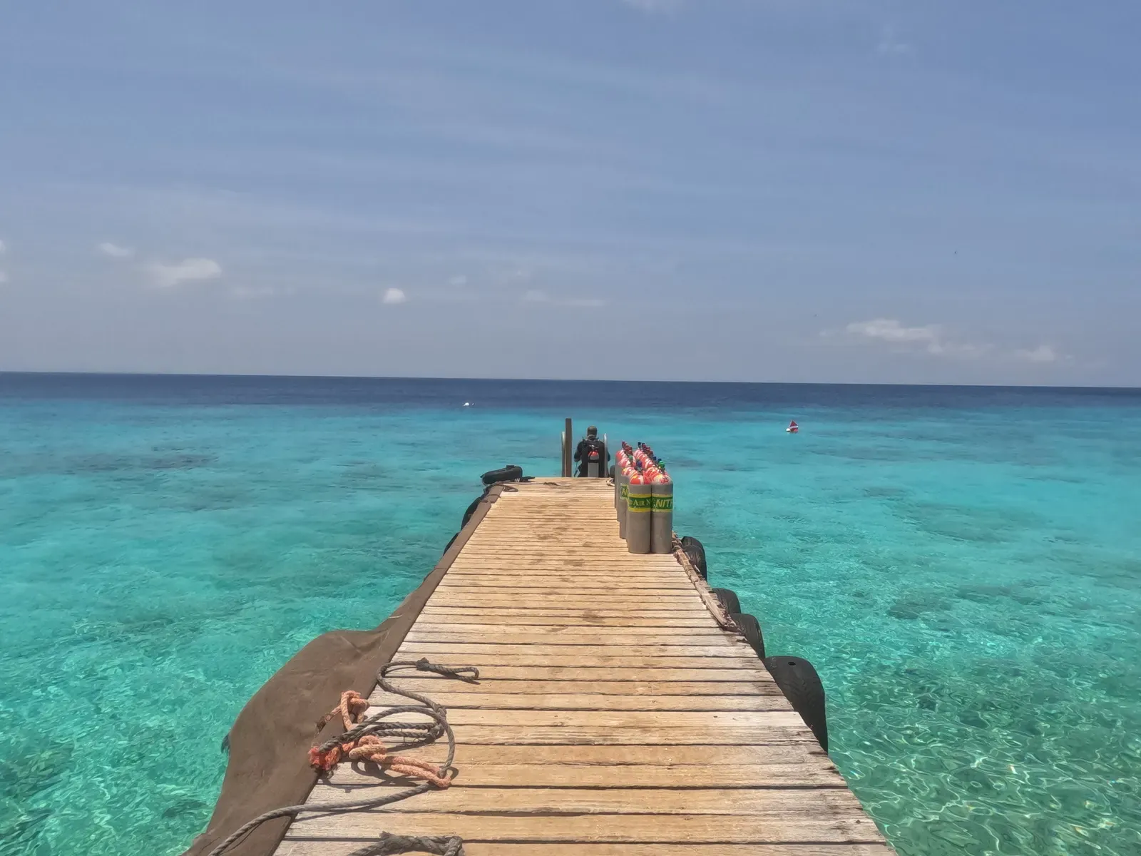A wooden dive pier stacked with scuba tanks runs out over turquoise water at Playa Kalki — Curaçao