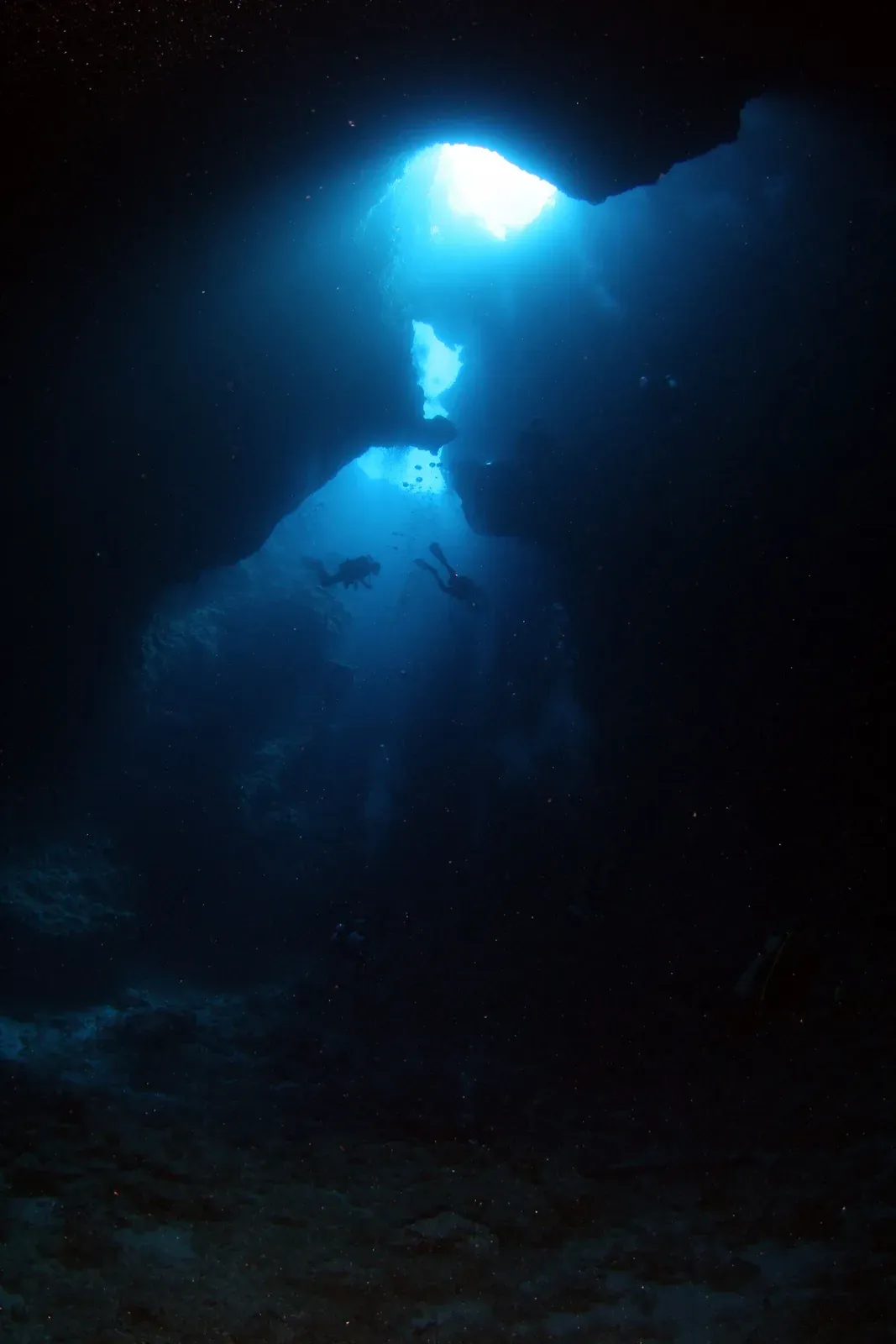 Divers silhouetted in a cavern beneath shafts of light falling through the entrance