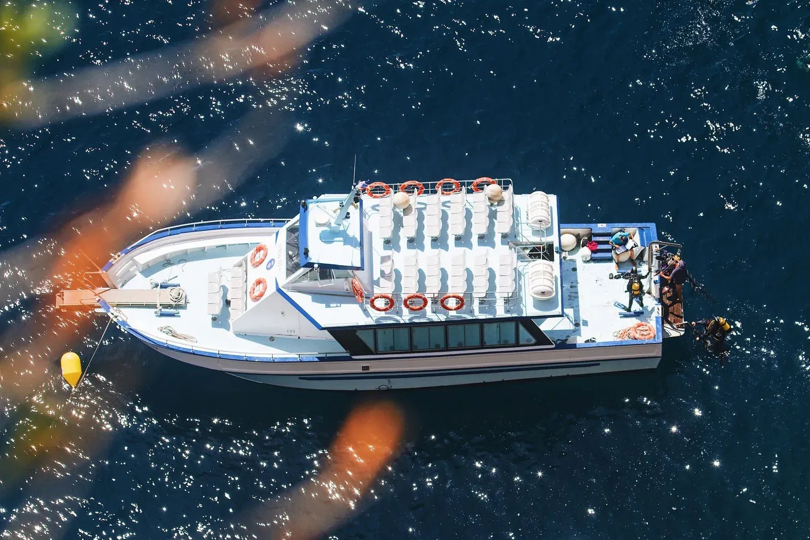 Aerial view of a dive boat with racked tanks and divers in the water off its stern