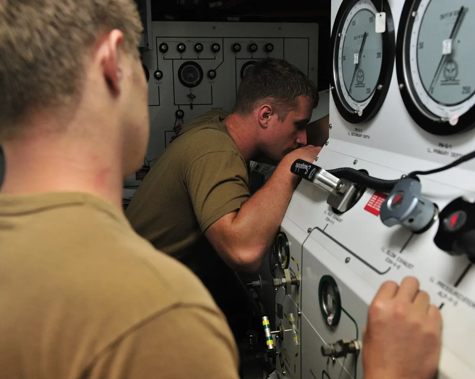 Two US Navy divers working the outside control panel of a recompression chamber, with two large depth gauges reading in feet of seawater above them