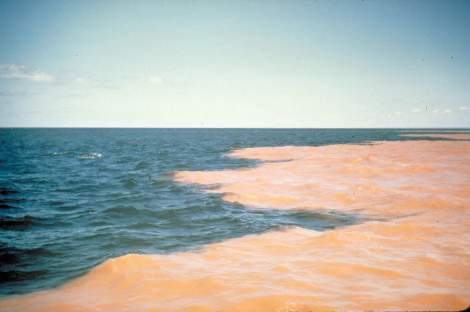 A sharp-edged band of red clay-laden water spreading across the blue surface of Lake Superior.