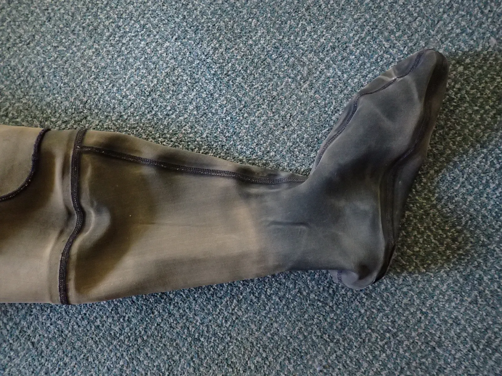 A drysuit leg with an integral neoprene sock, in mottled olive-grey crushed neoprene, laid on a blue speckled carpet.