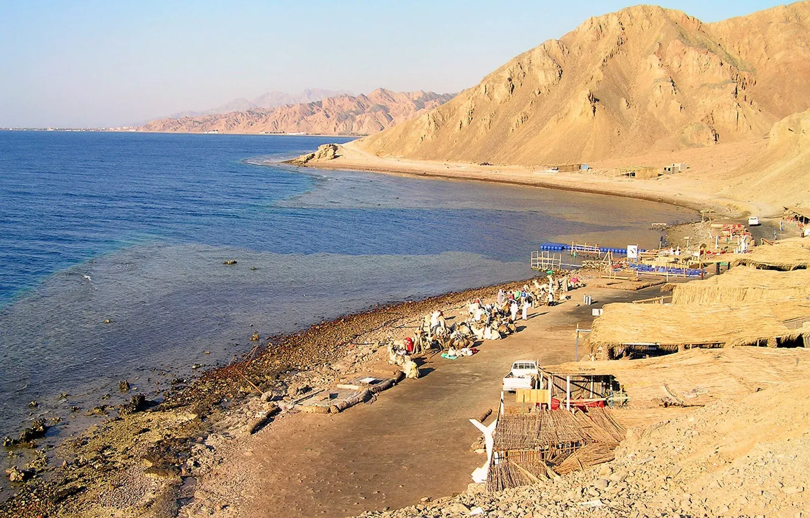 Dive camps and cafes on the stony shore at the Blue Hole north of Dahab, with the Sinai mountains behind and deep blue water beyond the reef edge