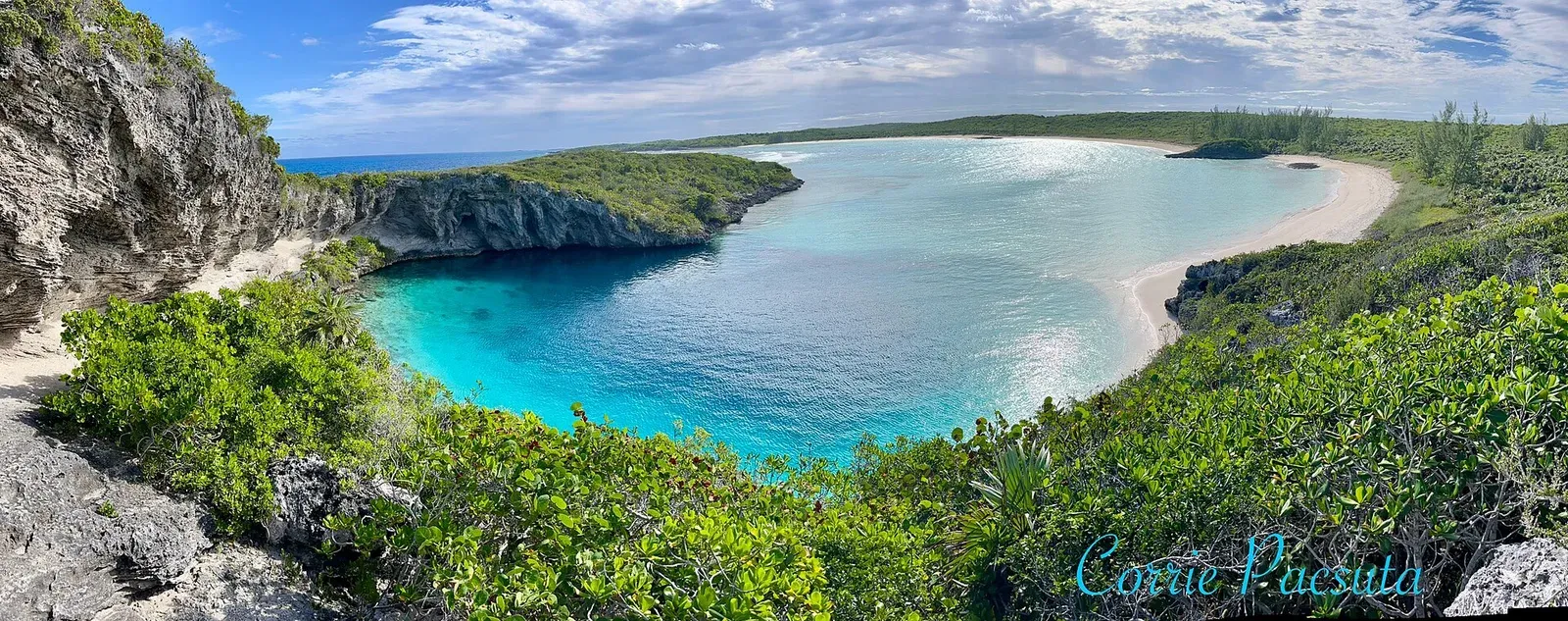 Dean's Blue Hole from the cliffs: a circle of deep blue water set against the turquoise shallows and white sand of a sheltered bay near Clarence Town
