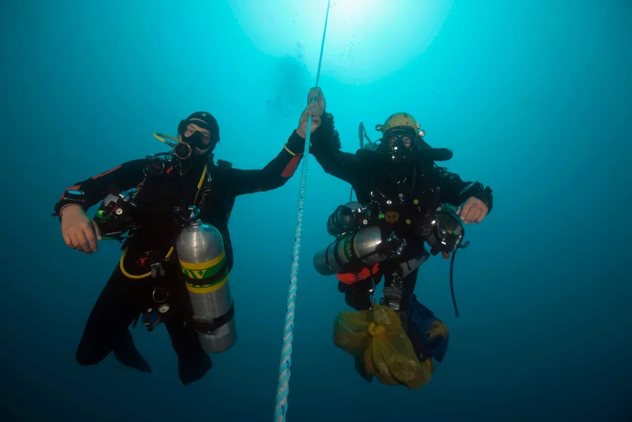 Two technical divers with stage cylinders holding a descent line in blue water, decompressing after a cave dive