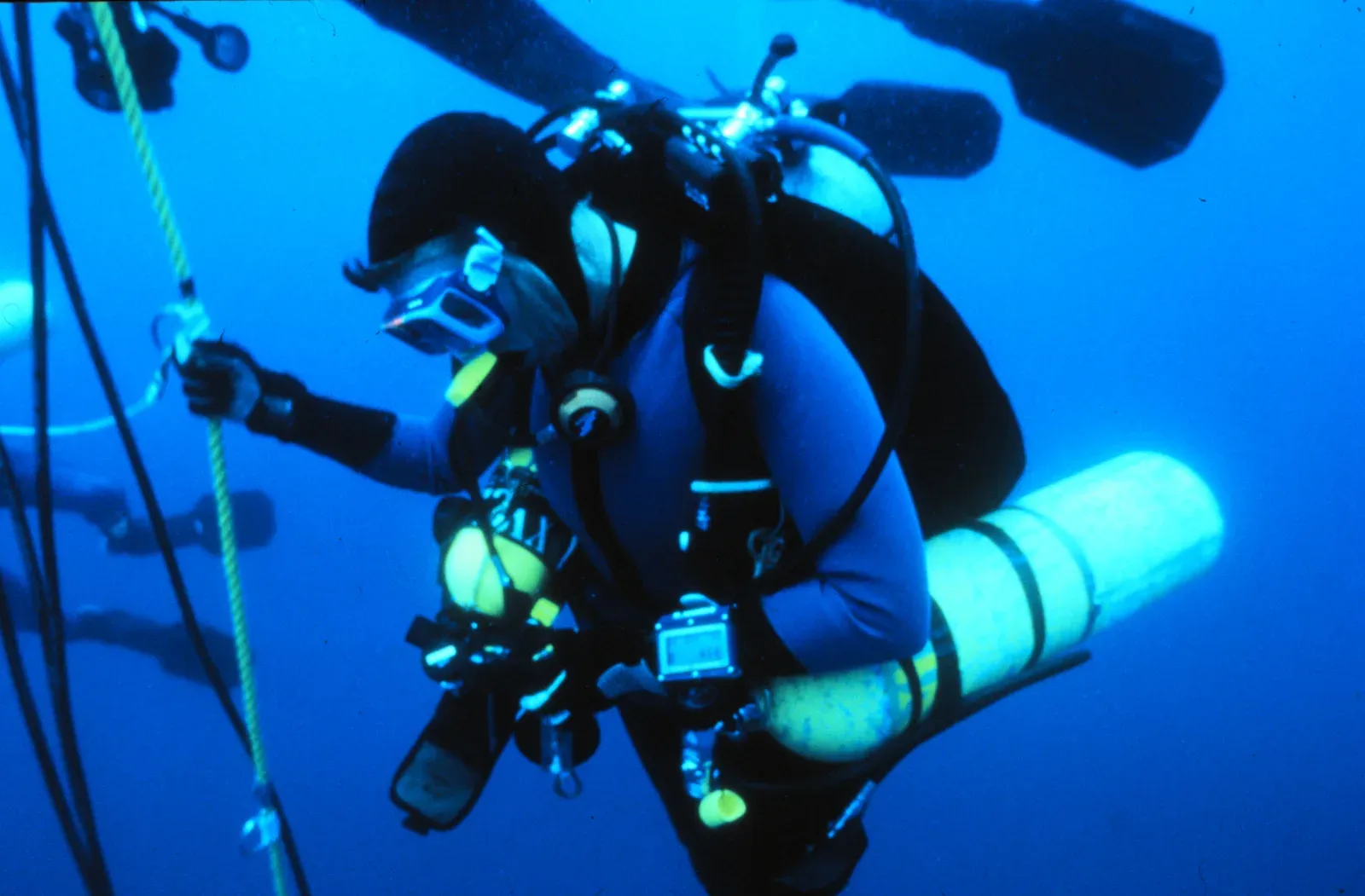 A technical diver on a shot line in blue water carrying slung decompression cylinders