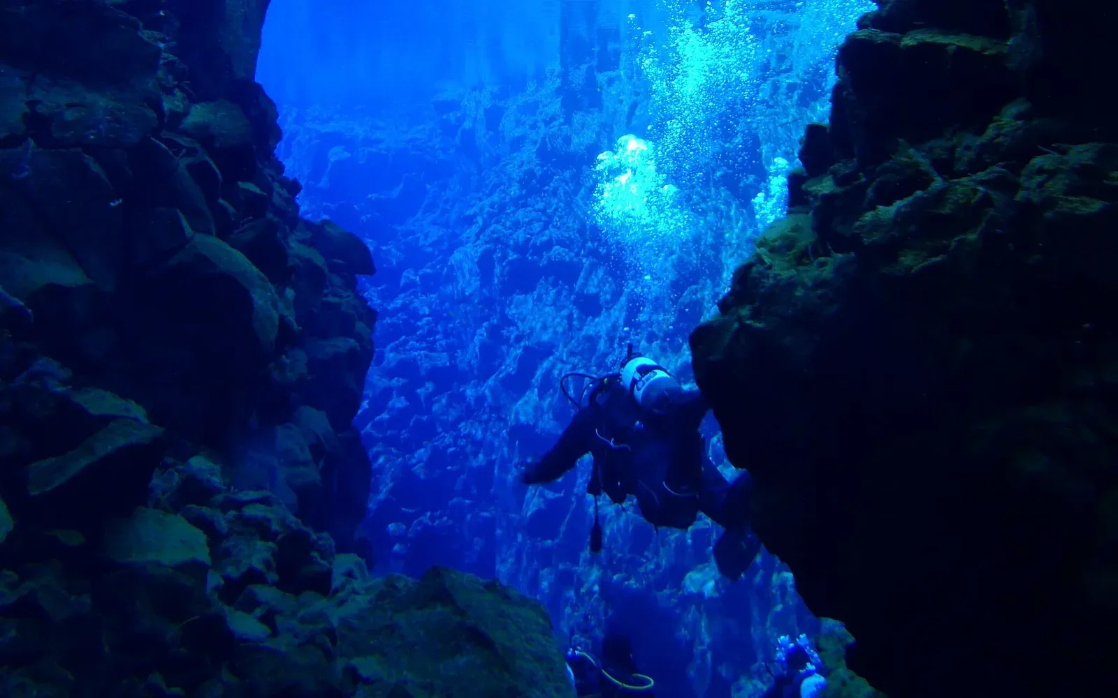 A diver descends between basalt walls in Iceland's Silfra fissure, the far rock still sharp through the blue meltwater.