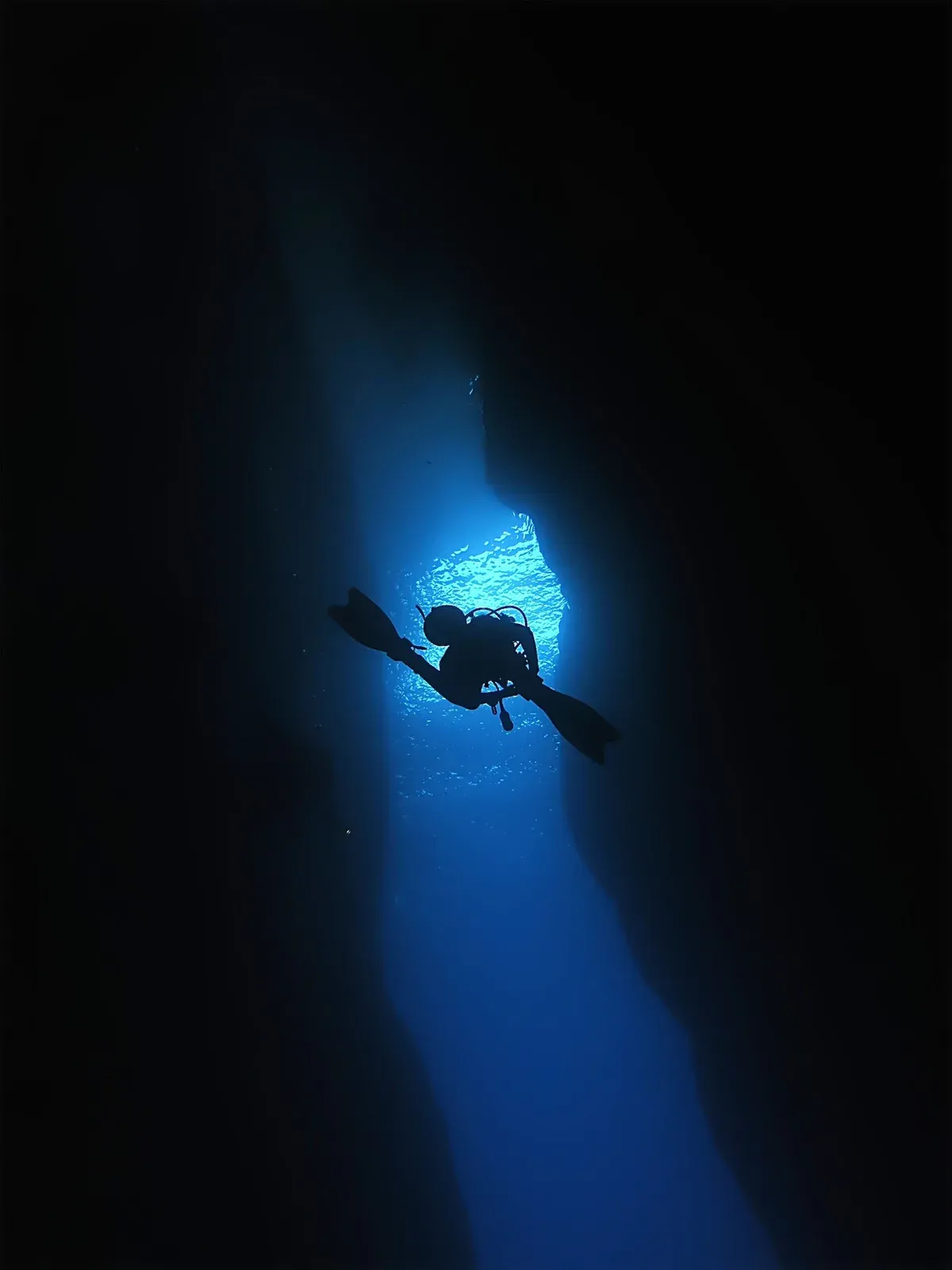 A diver in silhouette against the blue light at the end of a dark rock tunnel