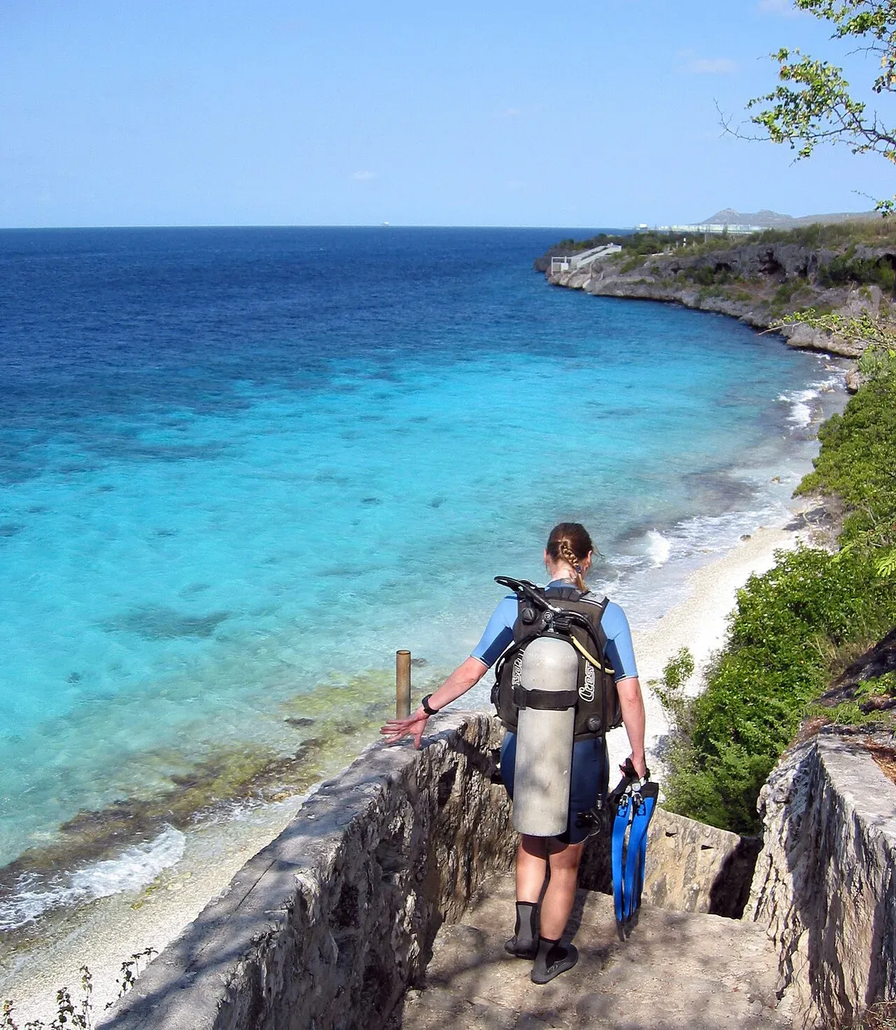 A diver in full kit walking down the stone steps at 1000 Steps on Bonaire towards turquoise water