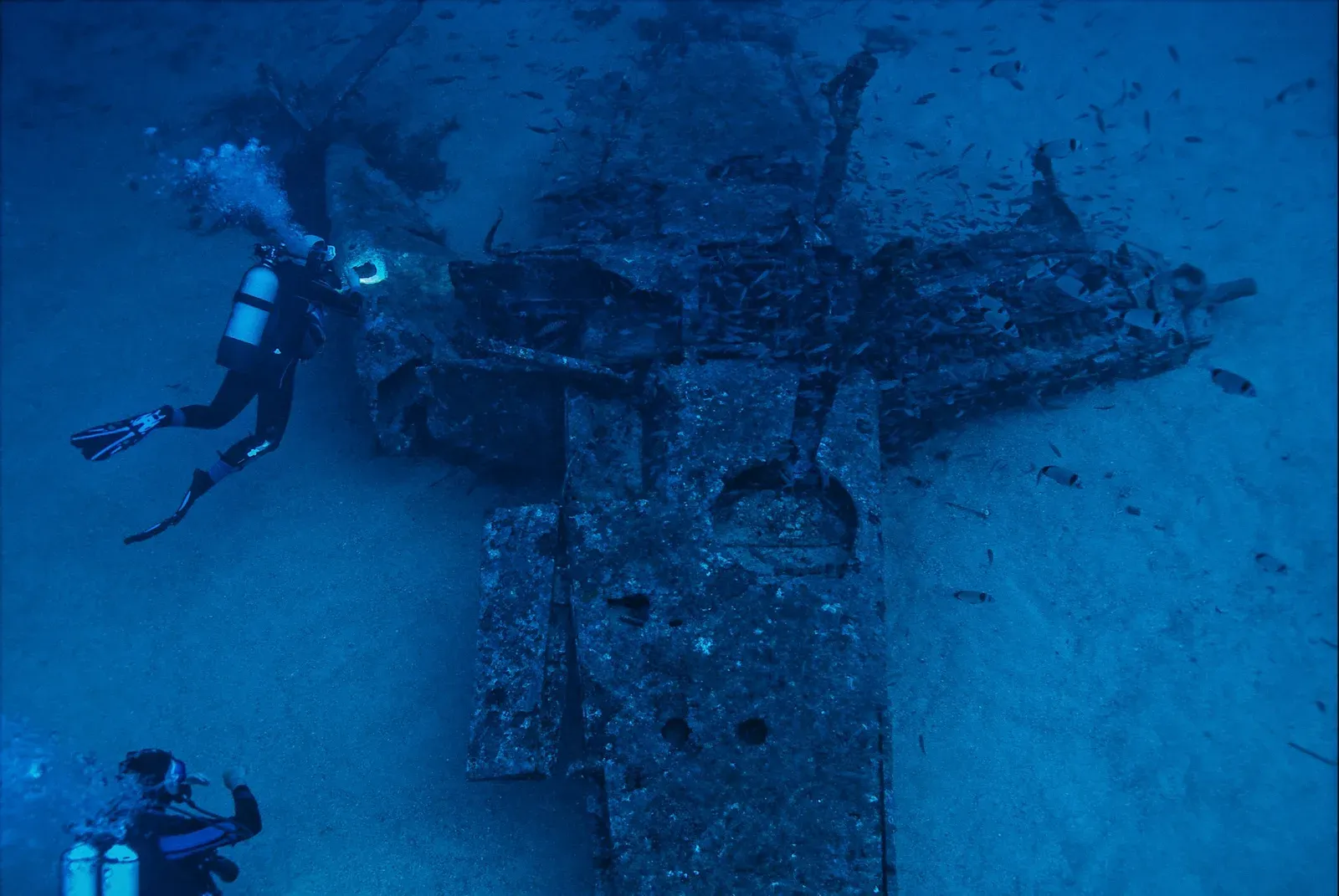 A diver pointing a torch at the wing of a sunken aircraft, with a second diver nearby