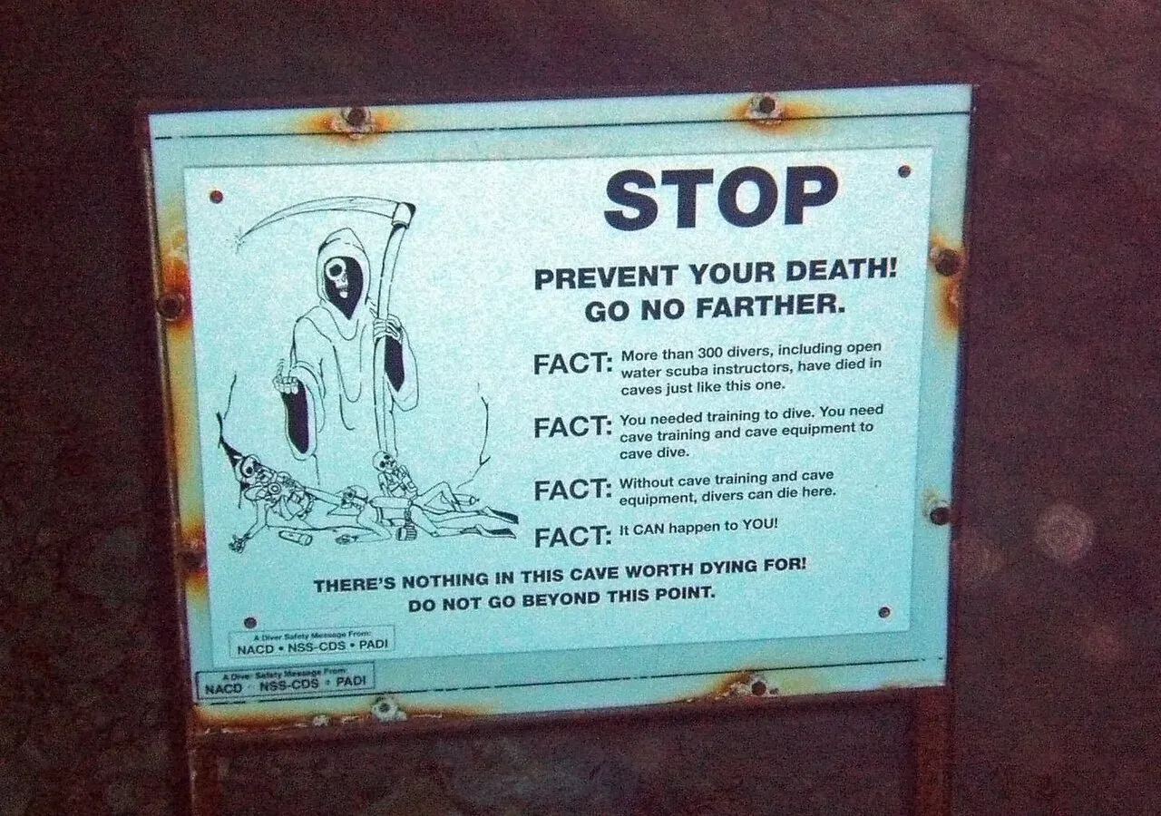 An underwater sign with a grim reaper drawing reading STOP, prevent your death, go no farther, at the cave entrance at Vortex Spring, Florida