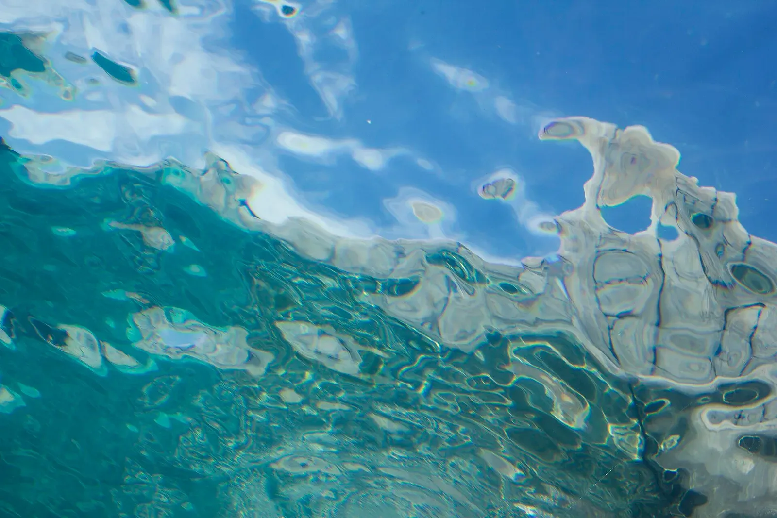 The rim of Snell's window seen from below: rippled blue sky above a wavy boundary, and beneath it the surface becomes a green-tinted mirror
